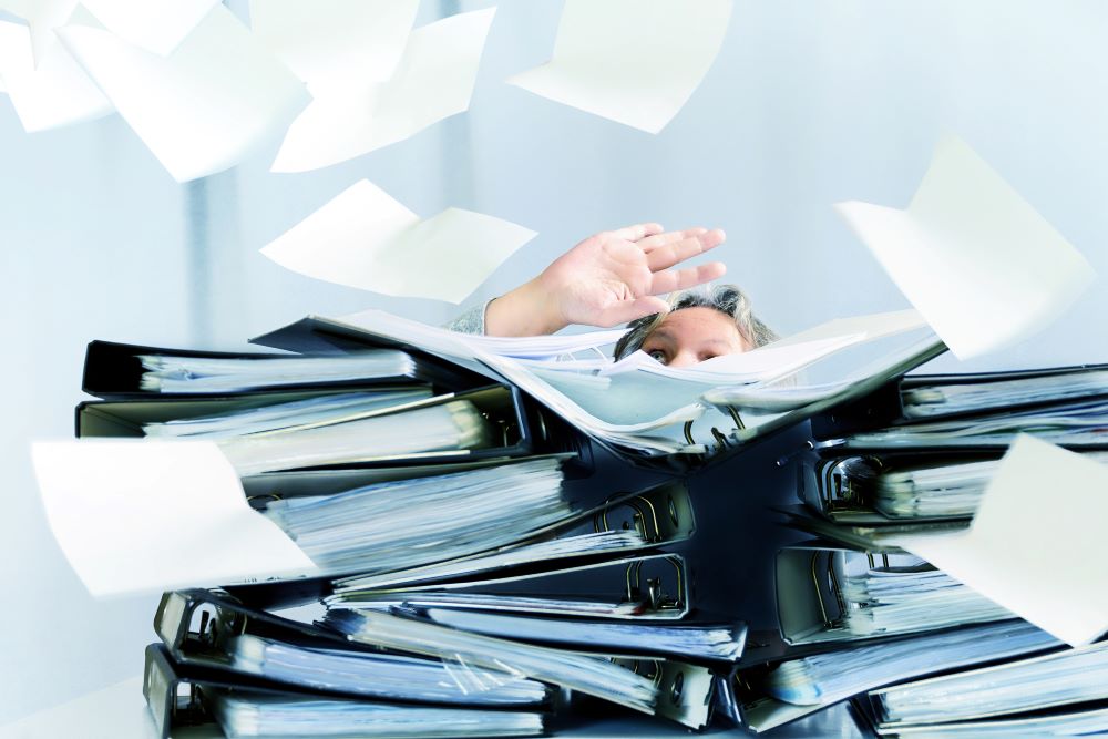 Close up image of a businessman surrounded by flying papers and binders signifying the need for a document management solution