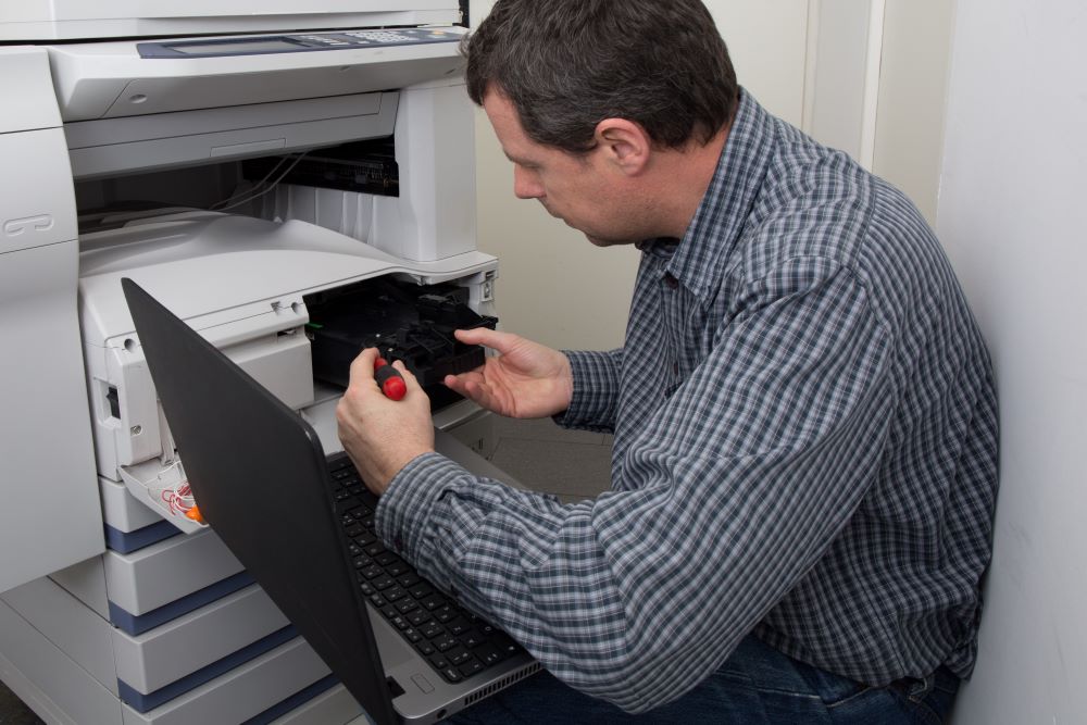 Technician works on an office multifunction printer signifying copier service.